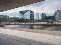 the city street has many buildings on it and a bridge across from it is under a cloudy sky