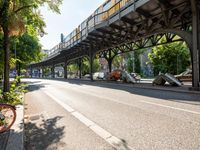 an overpass is an extension to an overpass on the street on which cars are parked on a narrow street with trees and buildings in the background