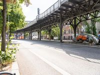 an overpass is an extension to an overpass on the street on which cars are parked on a narrow street with trees and buildings in the background