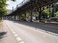 an overpass is an extension to an overpass on the street on which cars are parked on a narrow street with trees and buildings in the background