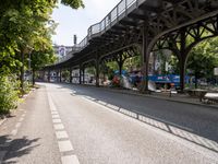 an overpass is an extension to an overpass on the street on which cars are parked on a narrow street with trees and buildings in the background