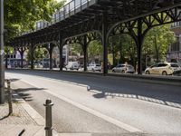 an overpass is an extension to an overpass on the street on which cars are parked on a narrow street with trees and buildings in the background