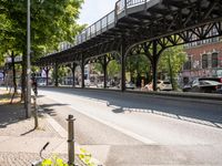 an overpass is an extension to an overpass on the street on which cars are parked on a narrow street with trees and buildings in the background