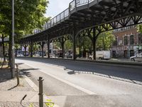 an overpass is an extension to an overpass on the street on which cars are parked on a narrow street with trees and buildings in the background