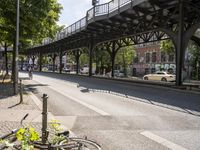 an overpass is an extension to an overpass on the street on which cars are parked on a narrow street with trees and buildings in the background