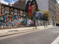 a wall with different colorful artwork on it in a city with buildings around and the street has a bike path going under it