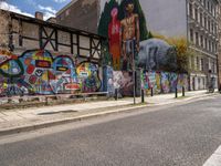 a wall with different colorful artwork on it in a city with buildings around and the street has a bike path going under it