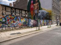 a wall with different colorful artwork on it in a city with buildings around and the street has a bike path going under it