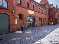 the streets are lined with brick buildings, cobblestone and plants, near doors and windows