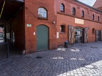 the streets are lined with brick buildings, cobblestone and plants, near doors and windows