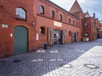 the streets are lined with brick buildings, cobblestone and plants, near doors and windows