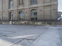 an empty parking lot next to the side of a large brown brick building with two doors