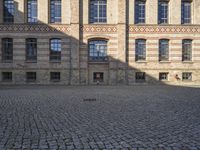 a group of large buildings with several windows and doors are standing on the cobblestones