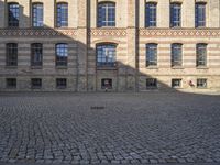 a group of large buildings with several windows and doors are standing on the cobblestones