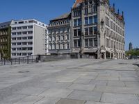 an empty building with a clock tower in it's middle block and a few people standing on the pavement