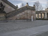 a brick walkway next to a building with stairs and columns on it in the afternoon