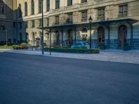 the building has arches and doors, but some blue cars are parked in front of it