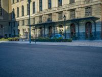 the building has arches and doors, but some blue cars are parked in front of it