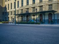 the building has arches and doors, but some blue cars are parked in front of it