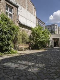 an empty cobblestone street in front of an old building with a bench on it