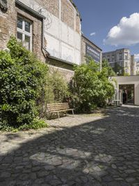 an empty cobblestone street in front of an old building with a bench on it