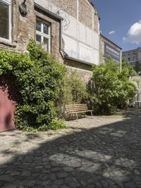 an empty cobblestone street in front of an old building with a bench on it