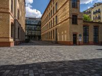 a sidewalk with chairs next to the brick building on the side, some have stairs and some buildings in the background