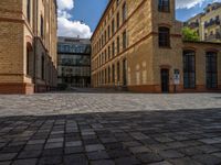 a sidewalk with chairs next to the brick building on the side, some have stairs and some buildings in the background