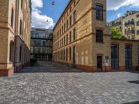 a sidewalk with chairs next to the brick building on the side, some have stairs and some buildings in the background