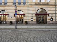 people walking on sidewalk in front of an old hotel building with large windows and doors