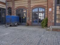 a blue trailer parked on the side of a brick road next to a building with a clock tower