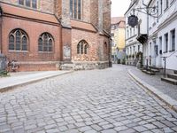 empty cobblestone paved street with a church in the background with brick buildings with bicycles on it