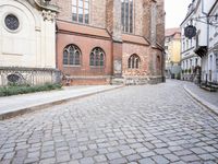 empty cobblestone paved street with a church in the background with brick buildings with bicycles on it