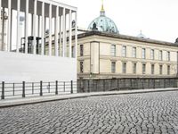 a city street is paved with cobblestone street in front of buildings and a clock