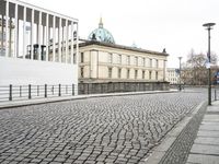 a city street is paved with cobblestone street in front of buildings and a clock