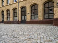 an old, brick courtyard has red bricks on it and windows in the background and a bench is beside the brick wall