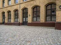 an old, brick courtyard has red bricks on it and windows in the background and a bench is beside the brick wall