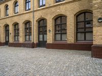 an old, brick courtyard has red bricks on it and windows in the background and a bench is beside the brick wall