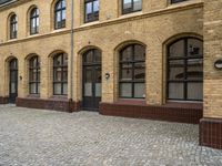 an old, brick courtyard has red bricks on it and windows in the background and a bench is beside the brick wall