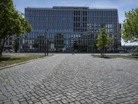 a man walks through a cobblestone area in front of a large glass building