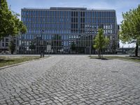 a man walks through a cobblestone area in front of a large glass building