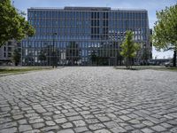 a man walks through a cobblestone area in front of a large glass building