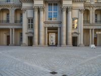 a courtyard with a building on the other side and a large white building with many windows