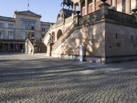 several steps with horses are on the cobblestones of an outdoor plaza with a large stone building in the background