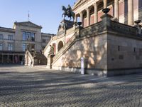 several steps with horses are on the cobblestones of an outdoor plaza with a large stone building in the background