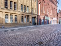 a cobblestone street has buildings and businesses on it, with an empty sidewalk