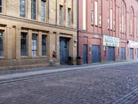 a cobblestone street has buildings and businesses on it, with an empty sidewalk