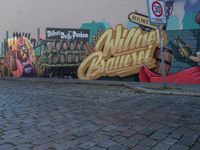 graffiti on wall, street corner, with sign and signpost near brick pavement, including wine barrels