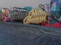 graffiti on wall, street corner, with sign and signpost near brick pavement, including wine barrels