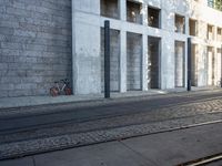 a street with a bike on the sidewalk in front of a building with windows and a woman in the foreground